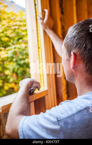 A man measuring the inside of a window frame on a residential house under construction. Stock Photo