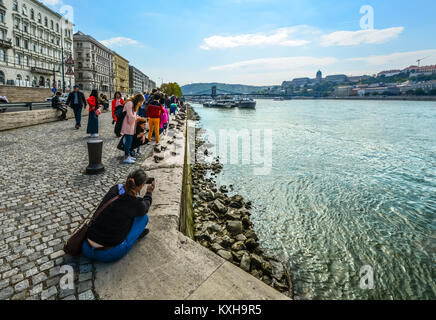The Shoes on the Danube Bank memorial to World War 2 victims in Budapest Hungary with boats on the river and tourists taking photos Stock Photo