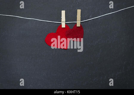 Two red hearts hanging from clothespin in front of chalkboard background Stock Photo