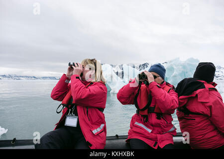 G Adventures cruise ship passengers watching wildlife using binoculars on a Zodiac dinghy in icy Arctic waters. Spitsbergen, Svalbard, Norway Stock Photo