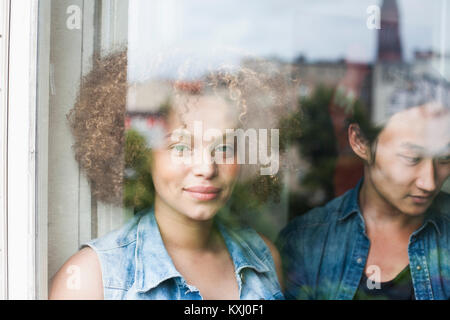 Portrait of smiling woman standing with man seen through glass window Stock Photo