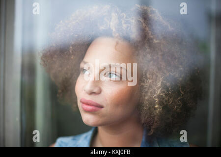Close-up of thoughtful woman with curly hair seen through glass window Stock Photo