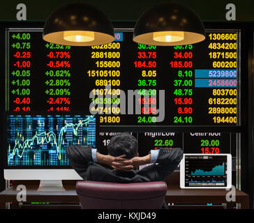 Back side of sitting businessman who is looking at big screen and desktop computer with tablet showing the trading graph of stock market exchange grap Stock Photo