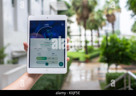Bangkok, Thailand - Aug 7, 2016 : Hand holding Apple ipad mini2 tablet showing the Pokemon Go application at screen over the walk way with park photo  Stock Photo