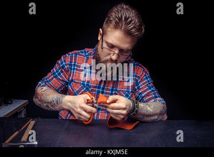 Craftsman working with leather works with leather goods at his desk Stock Photo