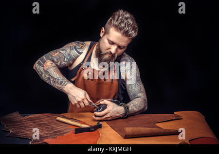 Young man, shoemaker, repairing old handmade shoe in his workshop and looking at the camera Stock Photo