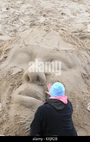 a sand sculptor or artist carving models and shapes out of the sand on the south bank shore of the river thames in London. Sand sculpture artistry. Stock Photo