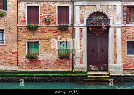 Facade of partially mossy old brick house with wooden vintage door on narrow canal in Venice, Italy. Stock Photo