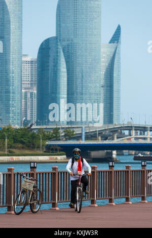 South Korean cyclist in front of Suyoung river with Centum park towers to the rear. Busan, South Korea. Stock Photo