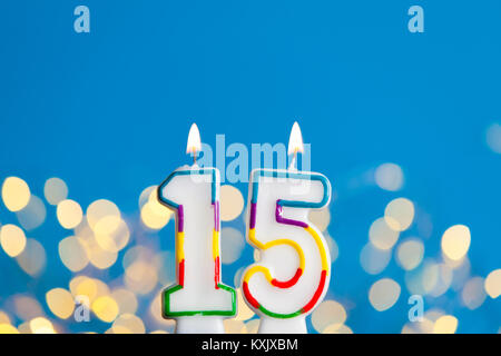 Number 15 birthday celebration candle against a bright lights and blue background Stock Photo