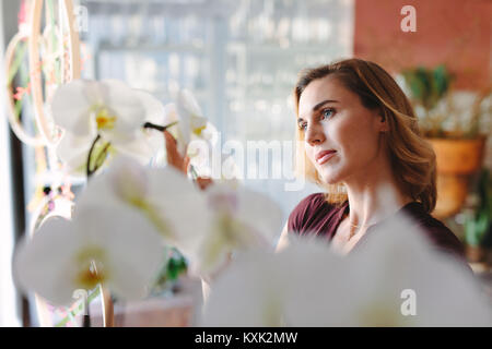 Thoughtful young florist owner standing in her own flower shop and looking away. Stock Photo