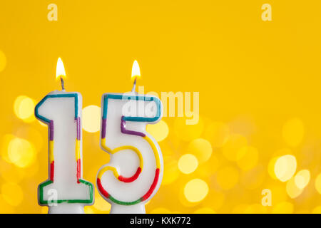 Number 15 birthday celebration candle against a bright lights and yellow background Stock Photo