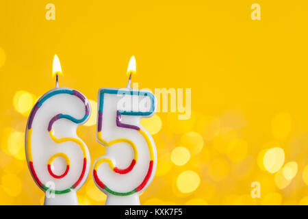 Number 65 birthday celebration candle against a bright lights and yellow background Stock Photo