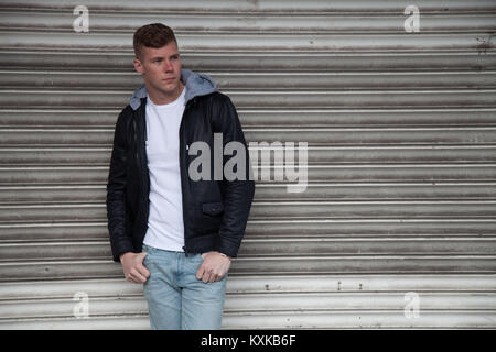 Good looking, blonde male model leaning on shop shutters in deserted shopping centre Stock Photo