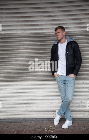 Good looking, blonde male model leaning on shop shutters in deserted shopping centre Stock Photo