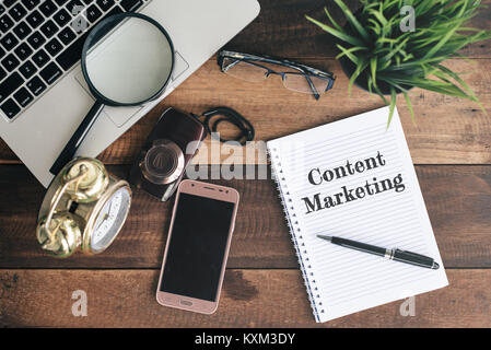 Laptop, magnifying glass, camera, phone, clock and notebook with CONTENT MARKETING word on a wooden table. content marketing concept Stock Photo