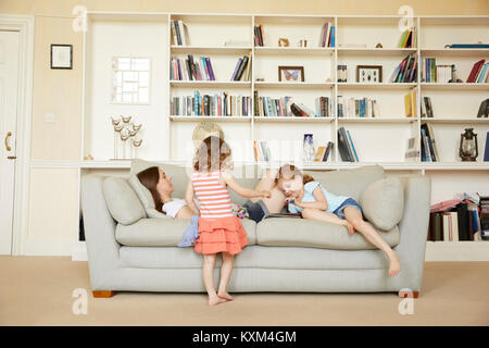 Woman reclining on sofa while daughters read storybook Stock Photo