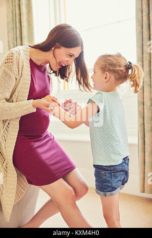 Laughing pregnant woman playing with daughter in living room Stock Photo