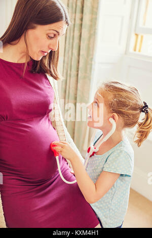 Girl with toy stethoscope listening to pregnant mother's stomach Stock Photo