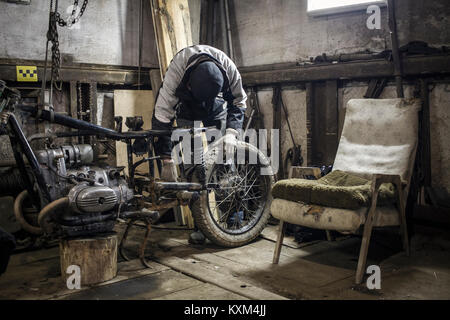 Mechanic adjusting wheel on dismantled vintage motorcycle in workshop Stock Photo