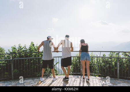 Rear view of three young adult friends looking out at lake Como from balcony,Como,Lombardy,Italy Stock Photo