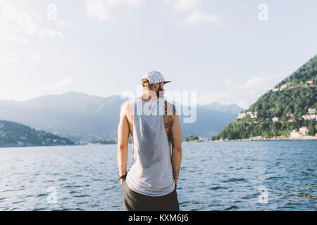 Rear view of young male hipster looking out from waterfront,Lake Como,Lombardy,Italy Stock Photo