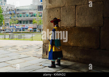A guard in historic outfit  stands looking out a modern city at Sungnyemun Gate also called Namdaemun Gate, Seoul, South Korea. Stock Photo