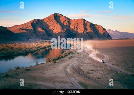 Dirt road cars racing dust cloud sunset landscape Mongolia red mountain river reflection Stock Photo