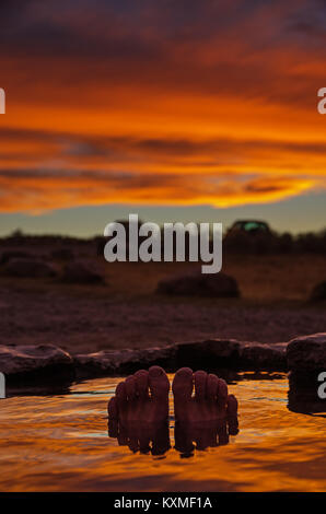 toes and feet poking out of a hot spring at sunset with reflection in the water and selective focus Stock Photo