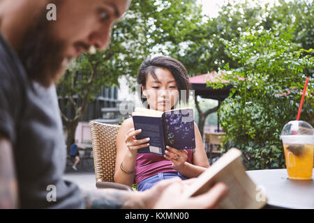 Multi ethnic hipster couple reading books at sidewalk cafe,Shanghai French Concession,Shanghai,China Stock Photo