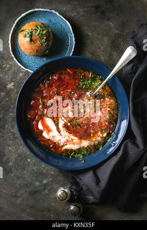 Plate of traditional beetroot borscht soup with sour cream, spoon and fresh coriander served with garlic bread buns pampushka with black textile napki Stock Photo