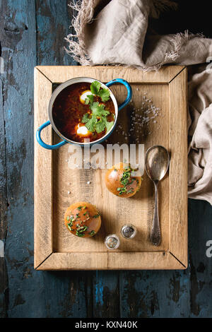 Pan of traditional beetroot borscht soup with sour cream and fresh coriander served with garlic bread buns pampushki, on wood tray with textile linen  Stock Photo