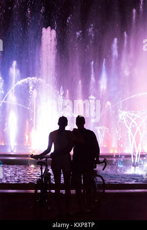 Hugging couple watching color fountain show at night Stock Photo