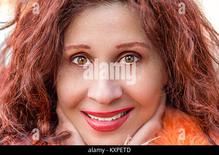 Extreme Close Up of a beautiful smiling deep eyes mature woman, Caucasian but with Arabic or Middle Eastern features, holding her chin with hands Stock Photo