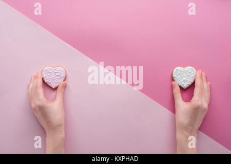 partial view of woman holding glazed cookies in hands on pink, st valentines day concept Stock Photo