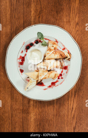 Top view of sweet crepe pancakes with jam and sour-cream on plate on wooden table Stock Photo