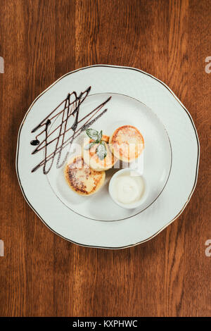 Top view of syrniki served on plate with sour-cream on wooden table Stock Photo