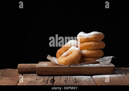 Sweet donuts with powdered sugar on a black background. Tasty, but harmful food on an old wooden table with copy space Stock Photo