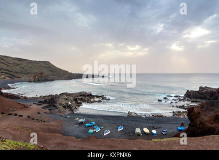wild beach on the Atlantic Ocean in El Golfo village. A rocky beach with fishing boats surrounded by volcanic mountains Stock Photo
