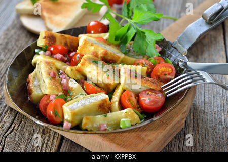 Fried Swabian meat ravioli (so called 'Maultaschen') with bacon and roasted cherry tomatoes served in an iron frying pan Stock Photo