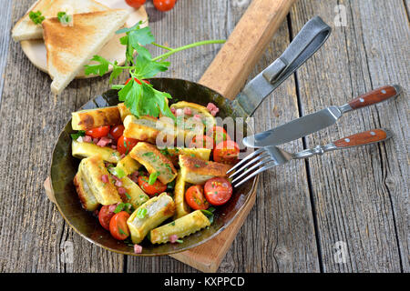 Fried Swabian meat ravioli (so called 'Maultaschen') with bacon and roasted cherry tomatoes served in an iron frying pan Stock Photo