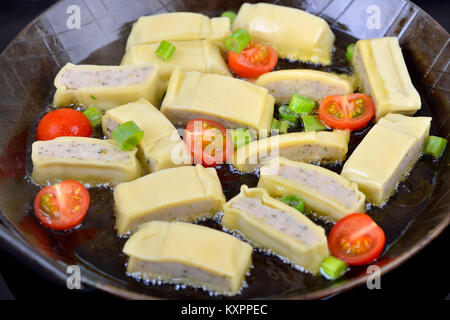Swabian meat ravioli (so called 'Maultaschen') cherry tomatoes and spring onions during frying in hot fat Stock Photo
