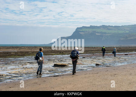 Walkers on the beach at Robin Hood's Bay, North Yorkshire, England. A sunny September morning looking towards Ravenscar. Stock Photo