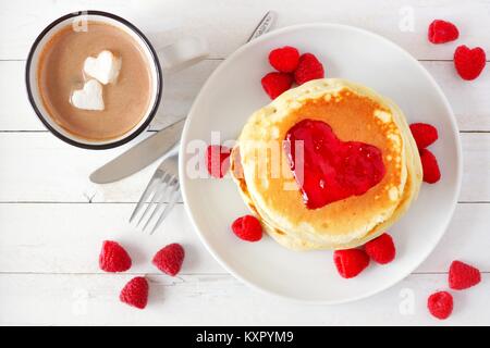 Pancakes with jam in shape of heart and hot chocolate with marshmallow hearts over a white wood table. Love concept. Stock Photo