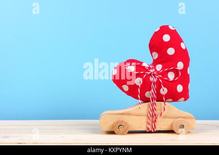 Wooden toy car carrying homemade heart gift against a blue background. Valentines Day or love concept. Stock Photo