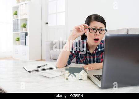 surprised pretty housewife looking at computer monitor feeling shocked when she finding family house tax very expensive. Stock Photo
