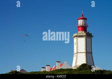 Red paraglider flying next to Cape Espichel lighthouse against a deep blue sky. Sesimbra, Portugal. Stock Photo