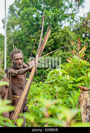 Korowai tribe. Papuan shooting arrows from a bow. Natural green jungle background. June 24, 2012 near Onni Village, New Guinea, Indonesia Stock Photo