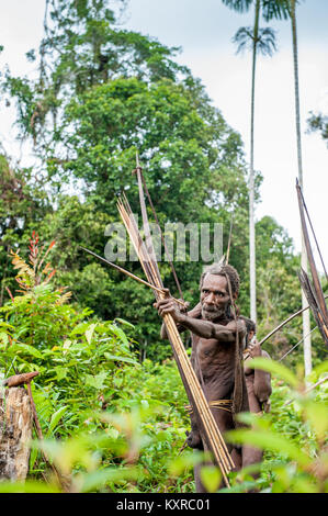 Korowai tribe. Papuan shooting arrows from a bow. Natural green jungle background. June 24, 2012 near Onni Village, New Guinea, Indonesia Stock Photo