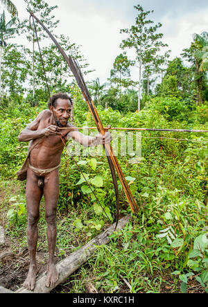 Korowai tribe. Papuan shooting arrows from a bow. Natural green jungle background. Stock Photo